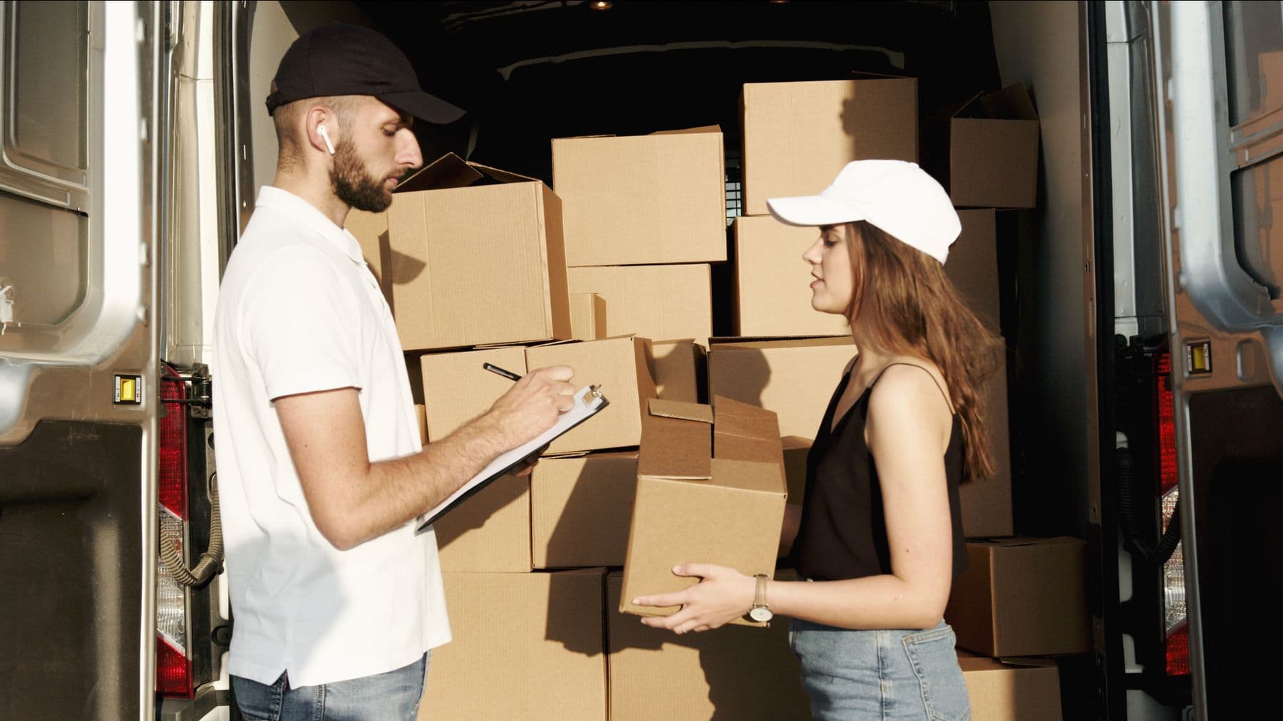 Two couriers sorting parcels in the back of a delivery van.