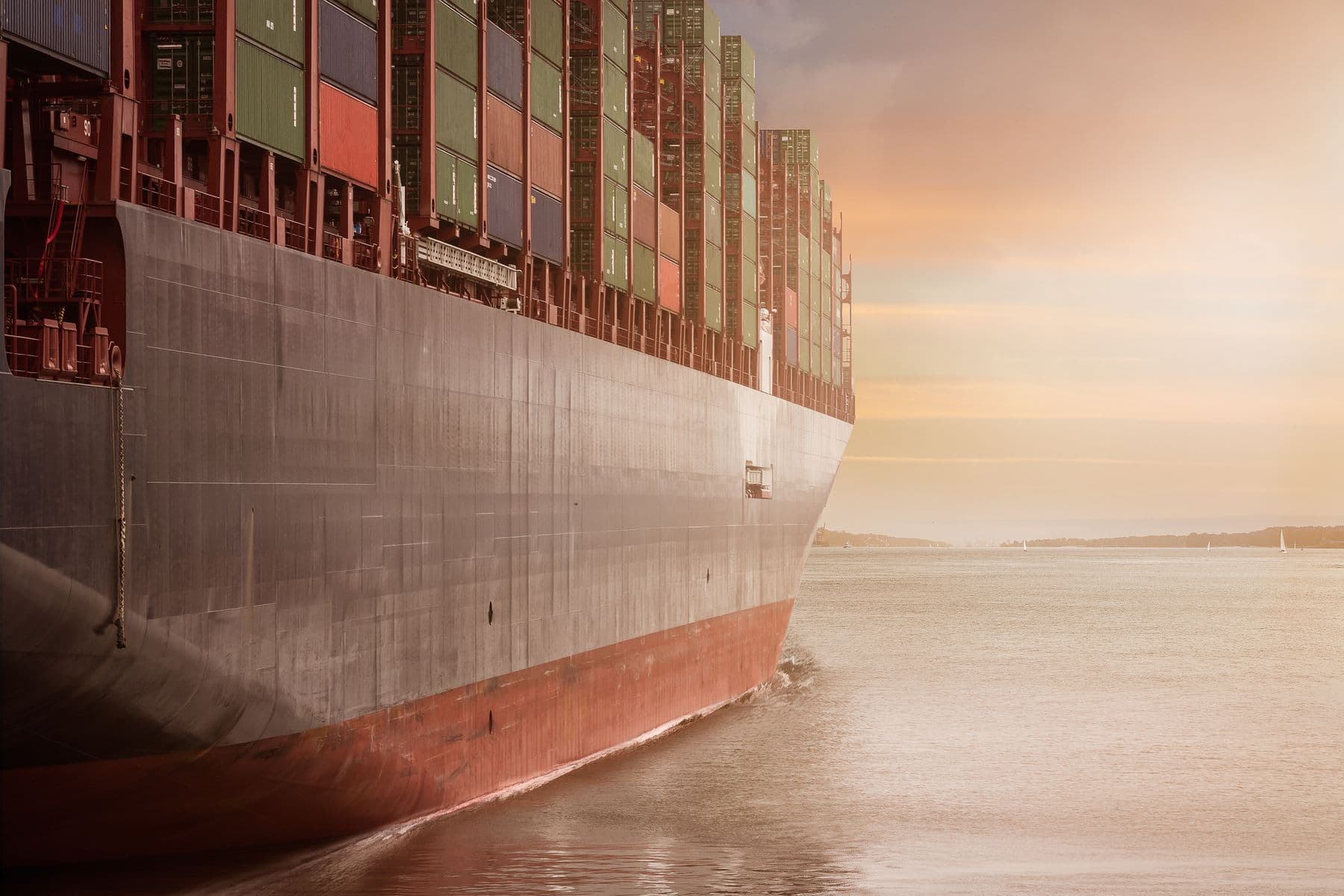 Fully laden container ship under way at sea against a warm sunset sky.